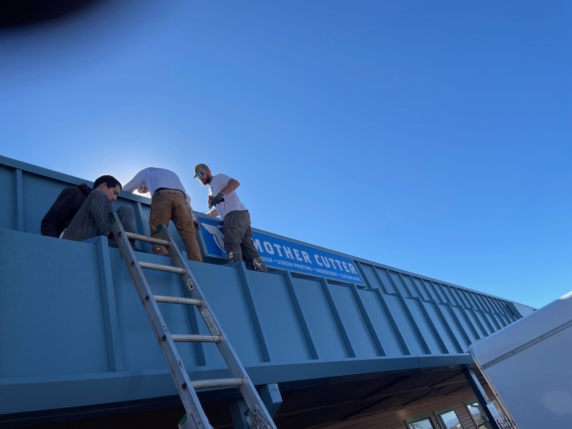 A group of men are painting a sign on the side of a building.