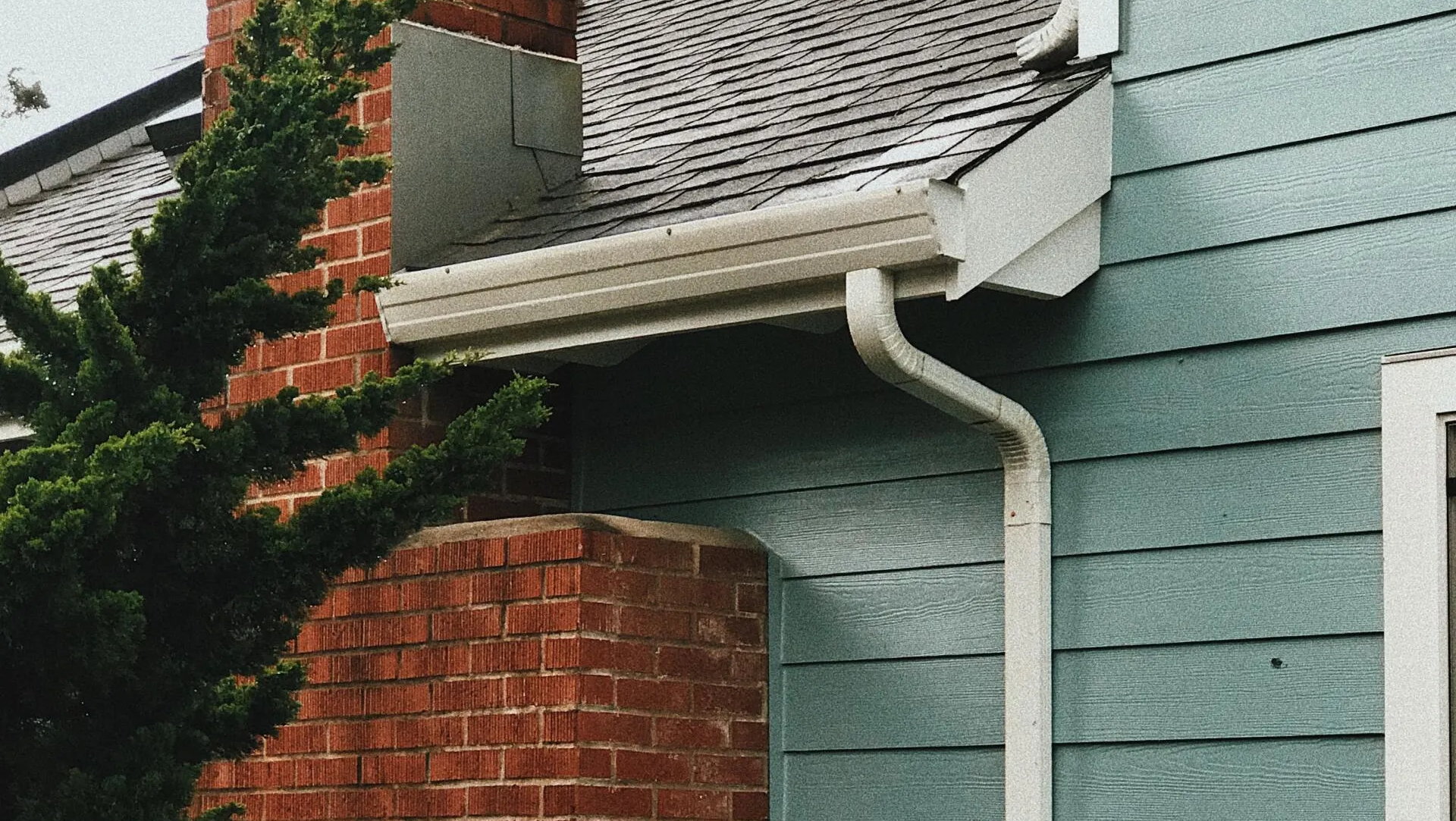A blue house with a white gutter and a brick chimney.