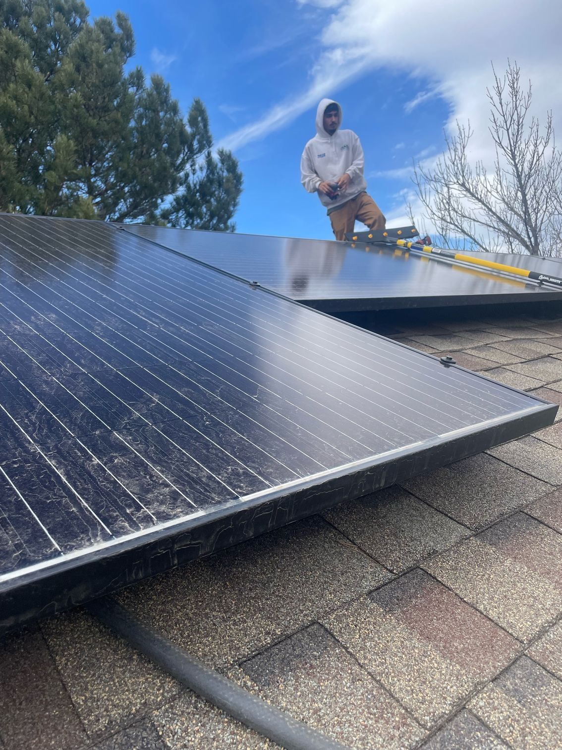 A man is standing on top of a roof with solar panels.