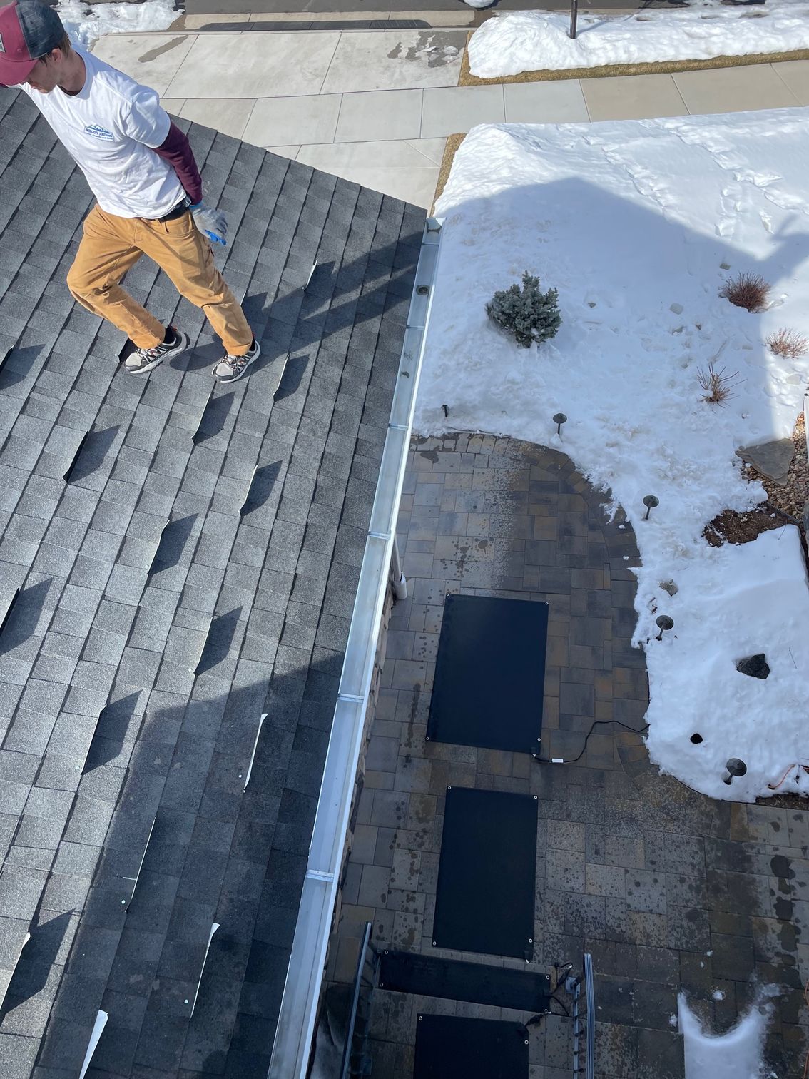 A man is standing on the roof of a house in the snow.