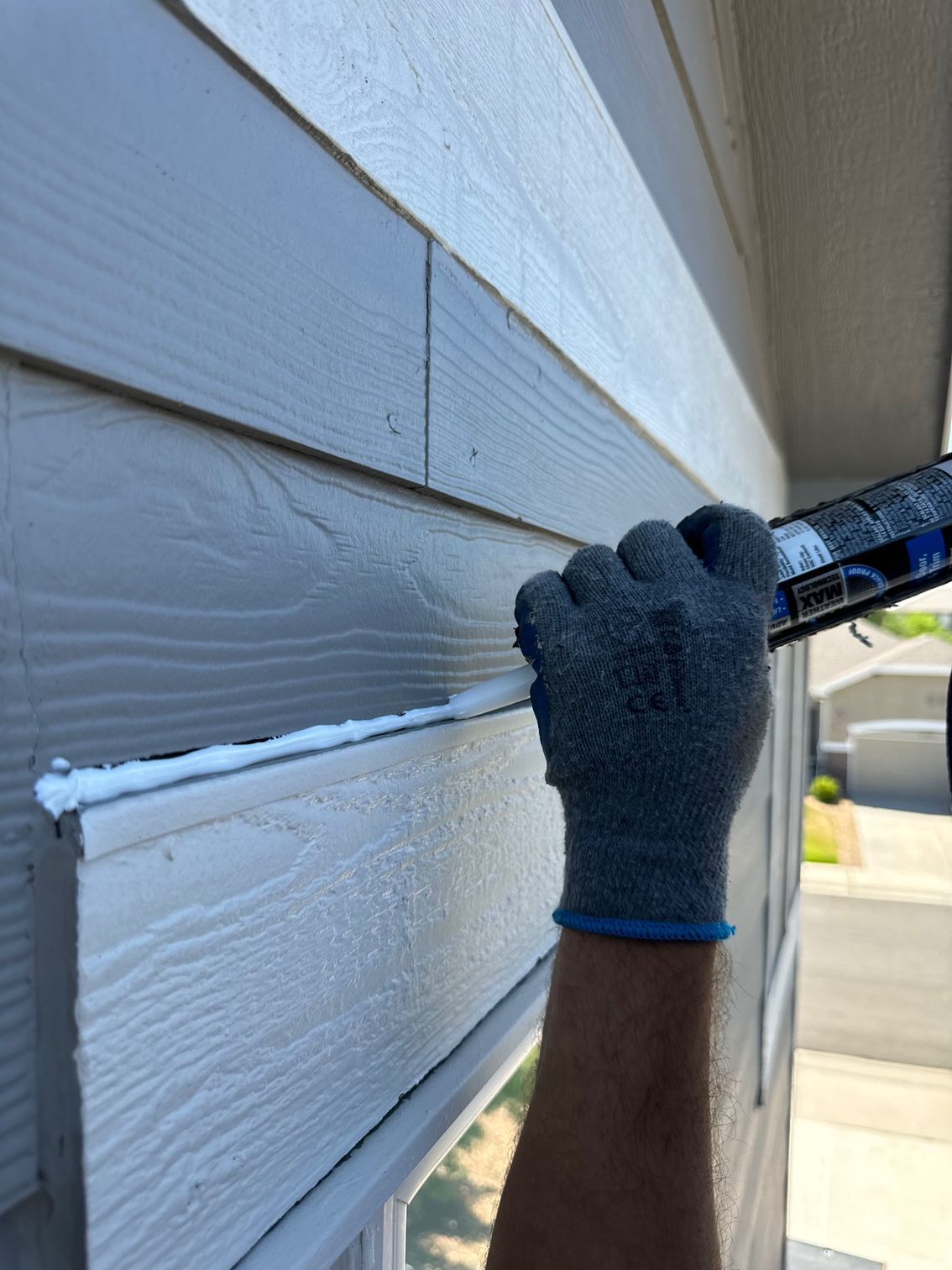 A person wearing a glove is applying silicone sealant to a house.