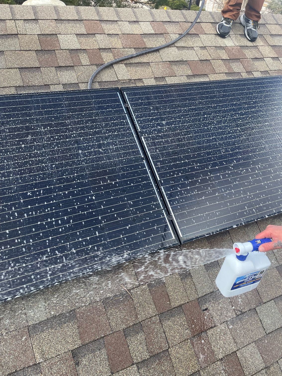 A person is spraying water on a solar panel on a roof.