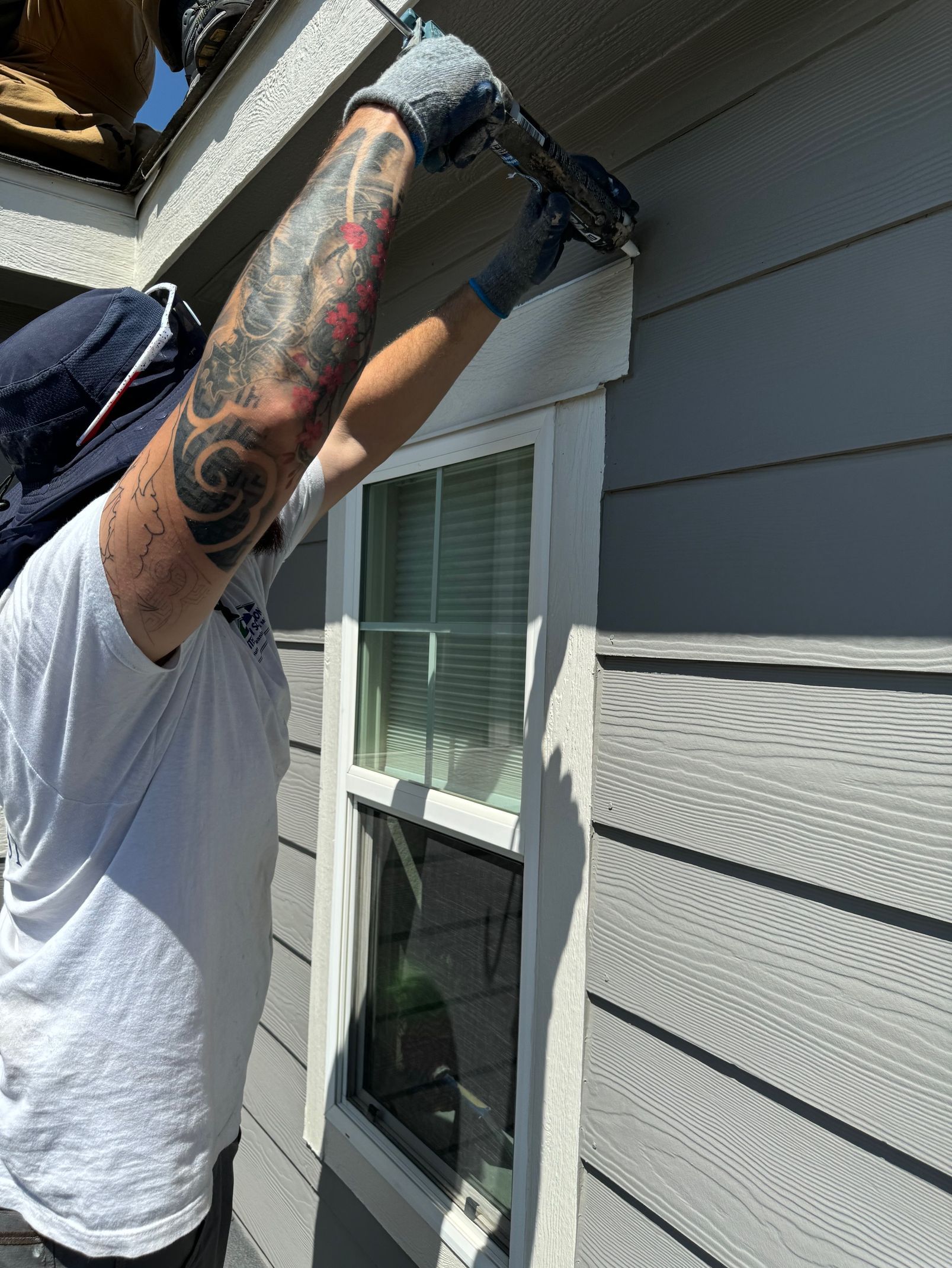 A man with a tattoo on his arm is working on the side of a house.