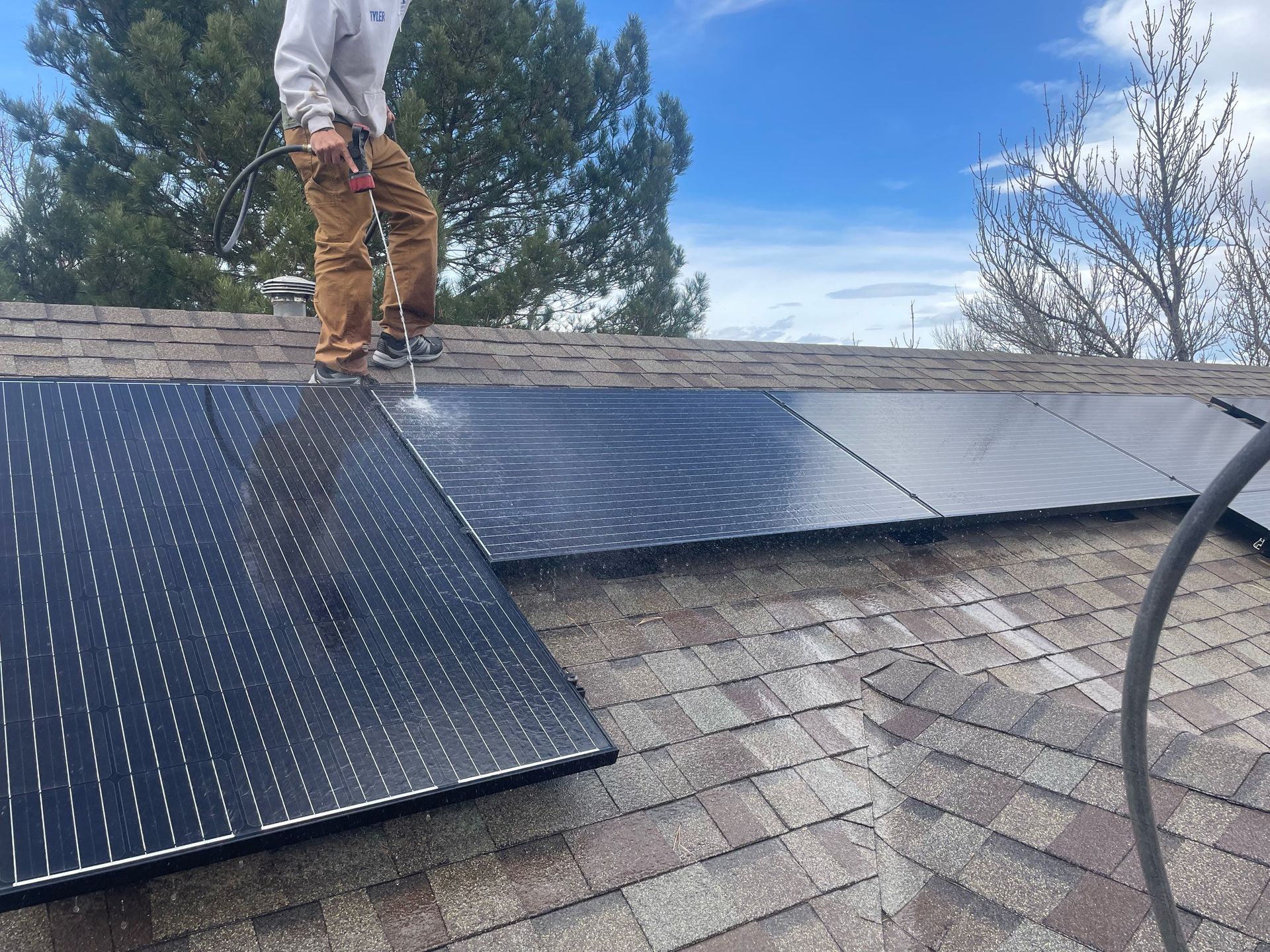 A man is standing on top of a roof cleaning solar panels.