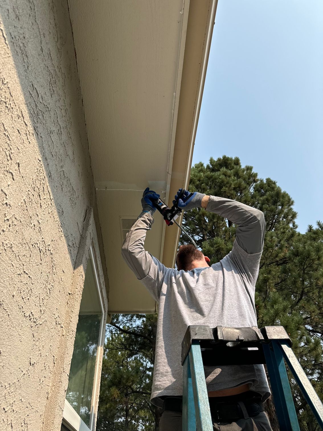 A man is standing on a ladder working on the roof of a house.