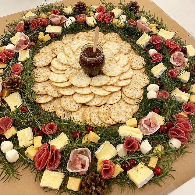 A wreath made of crackers cheese and flowers with a jar of jam in the center