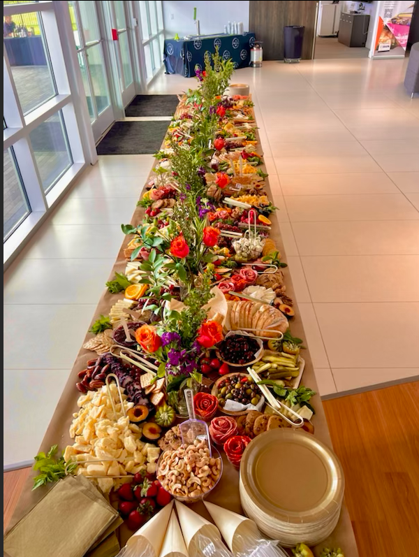 A wooden cutting board filled with fruits , cheeses , and flowers.