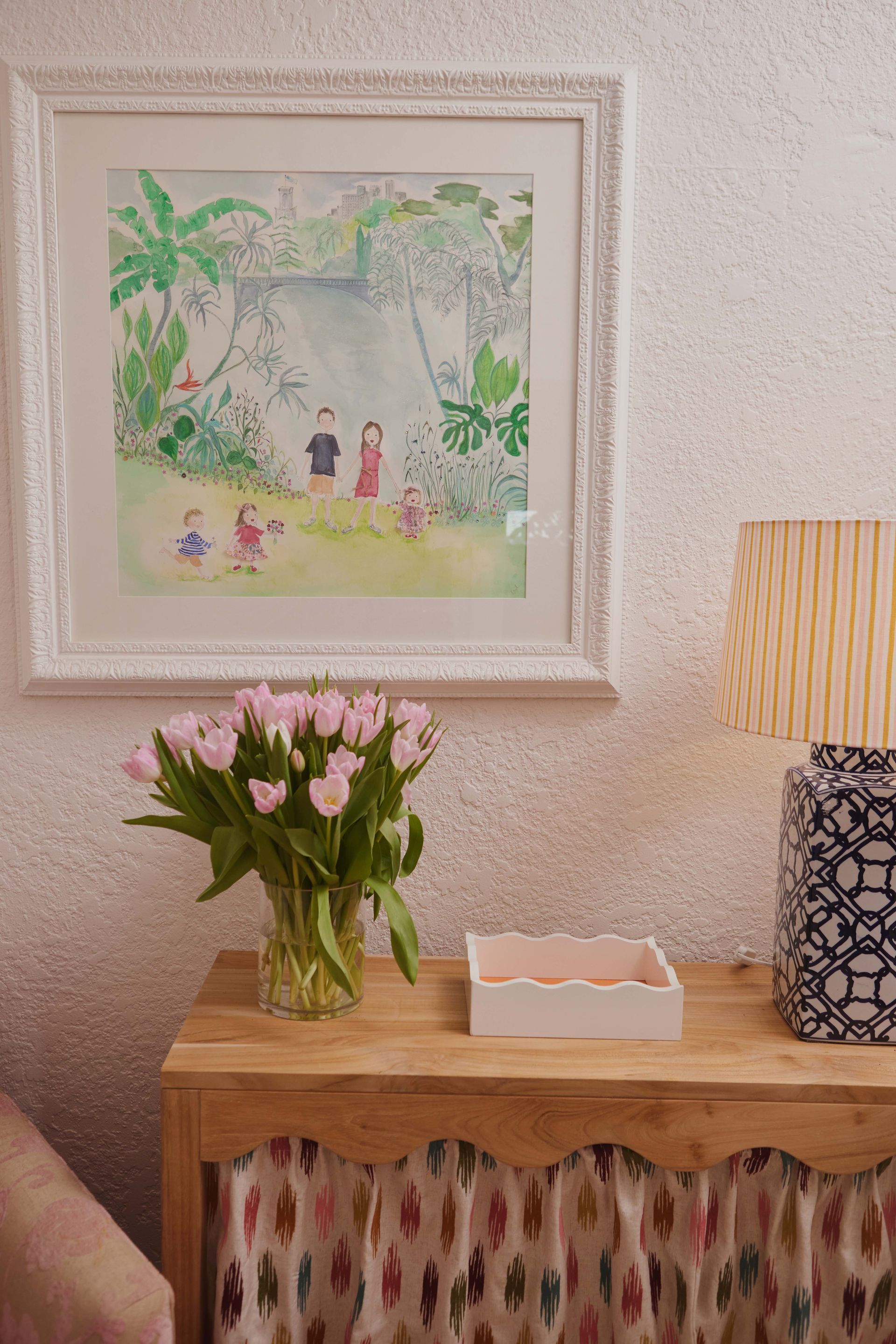 A table with a vase of flowers and a painting on the wall above it.