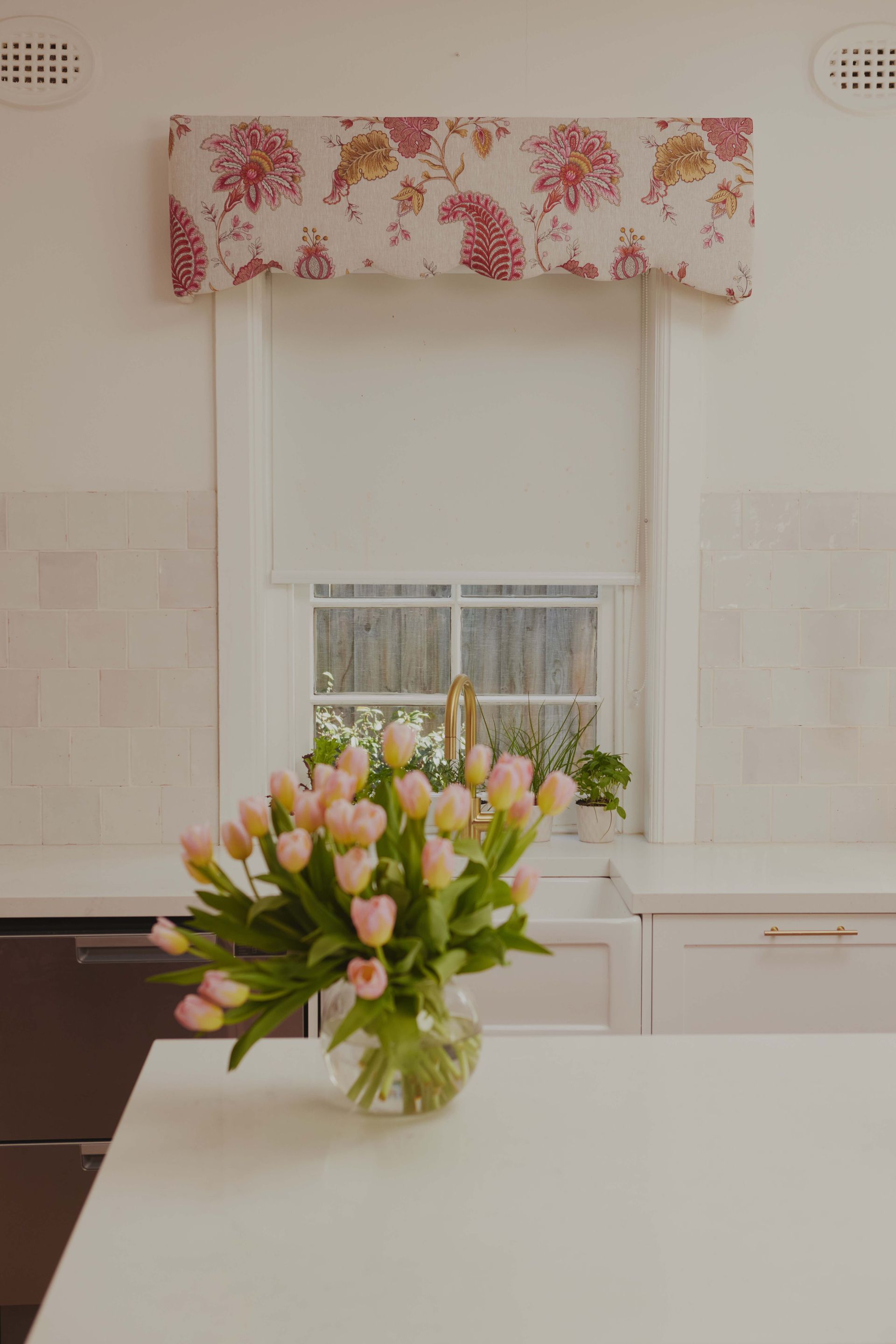 A vase of flowers is sitting on a table in front of a window in a kitchen.