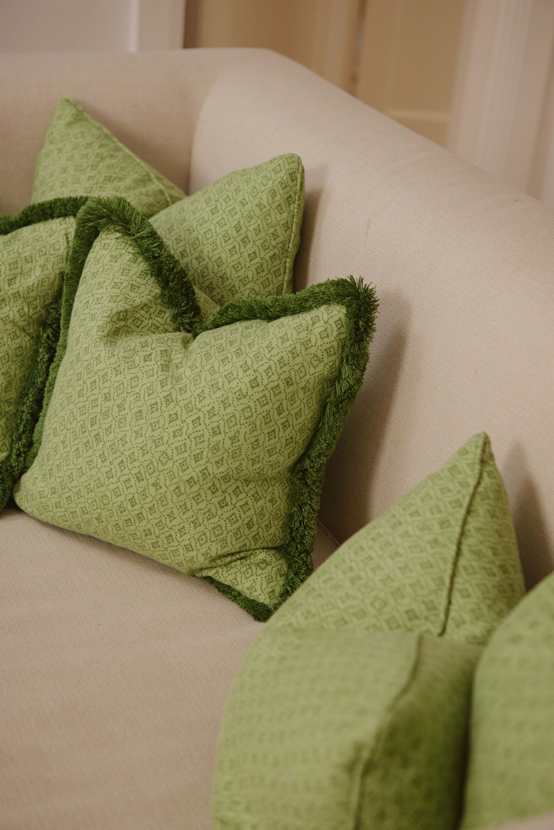 Three green pillows are sitting on a white couch.