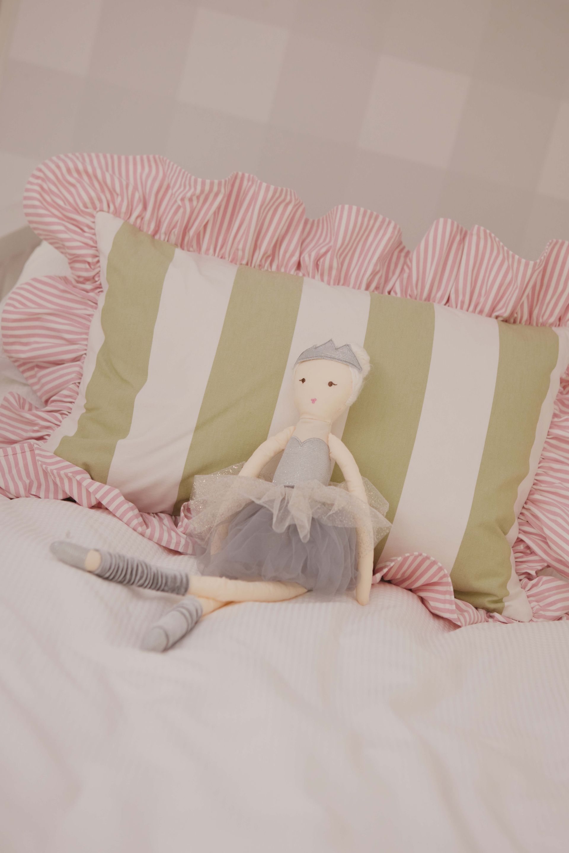 A doll is sitting on a bed next to a striped pillow.