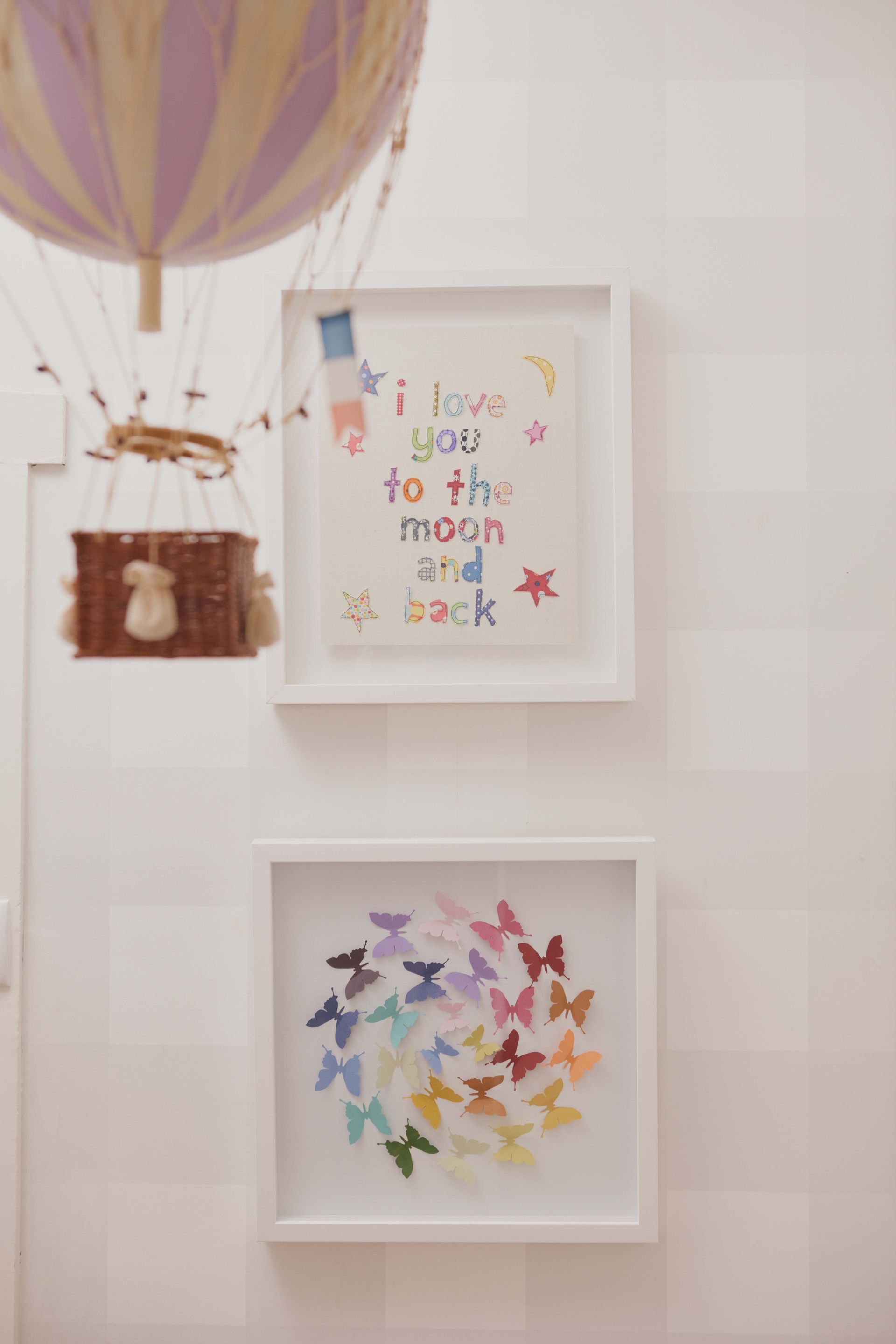 A hot air balloon is hanging from the ceiling above two framed pictures.