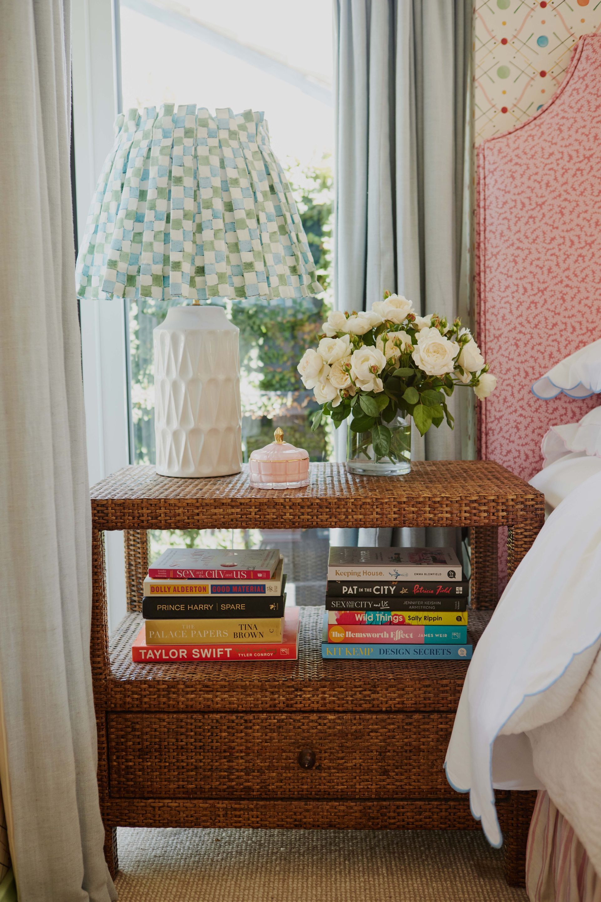 A nightstand with a lamp and books on it in a bedroom.