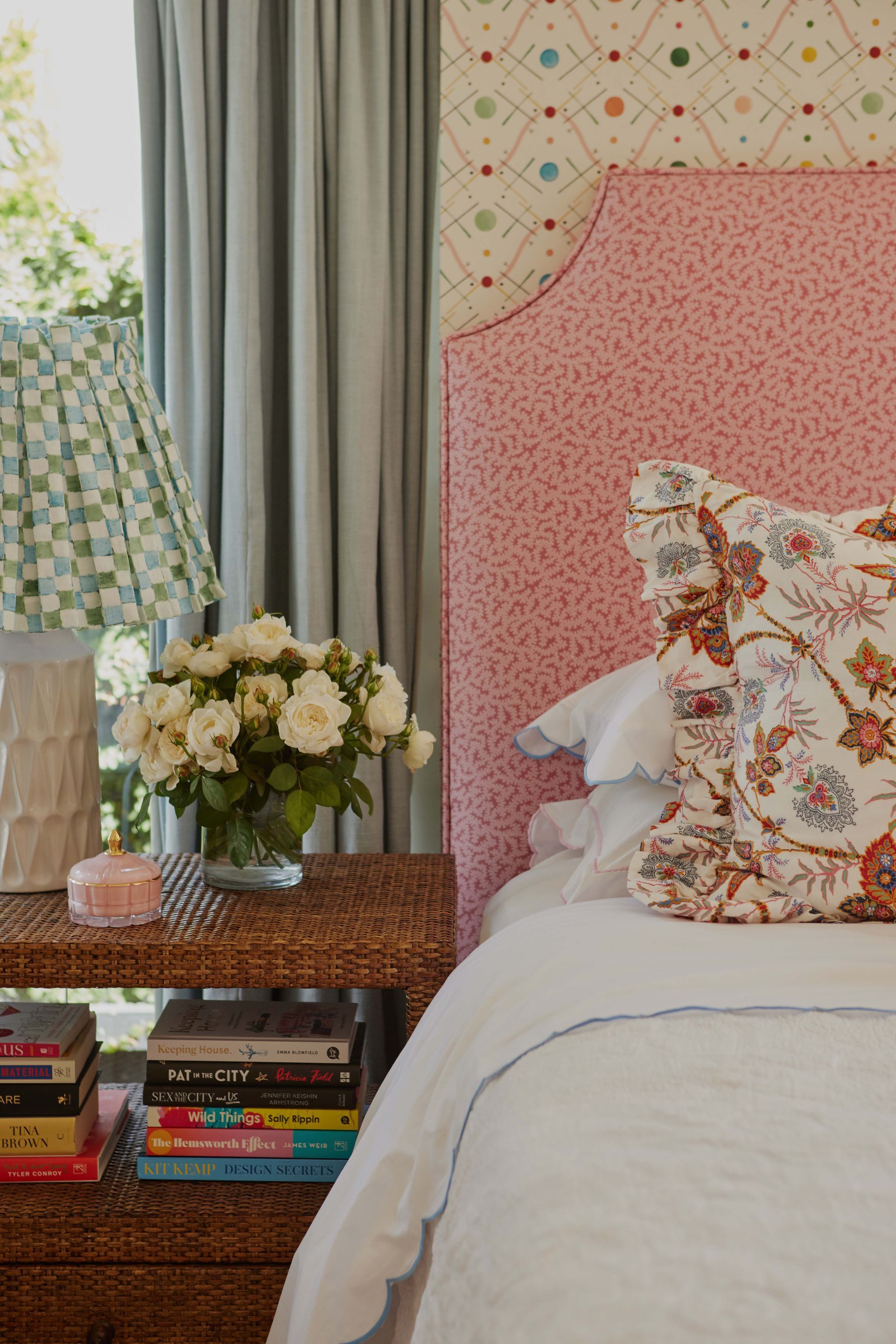 A bed with a pink headboard and a nightstand with books and flowers on it.