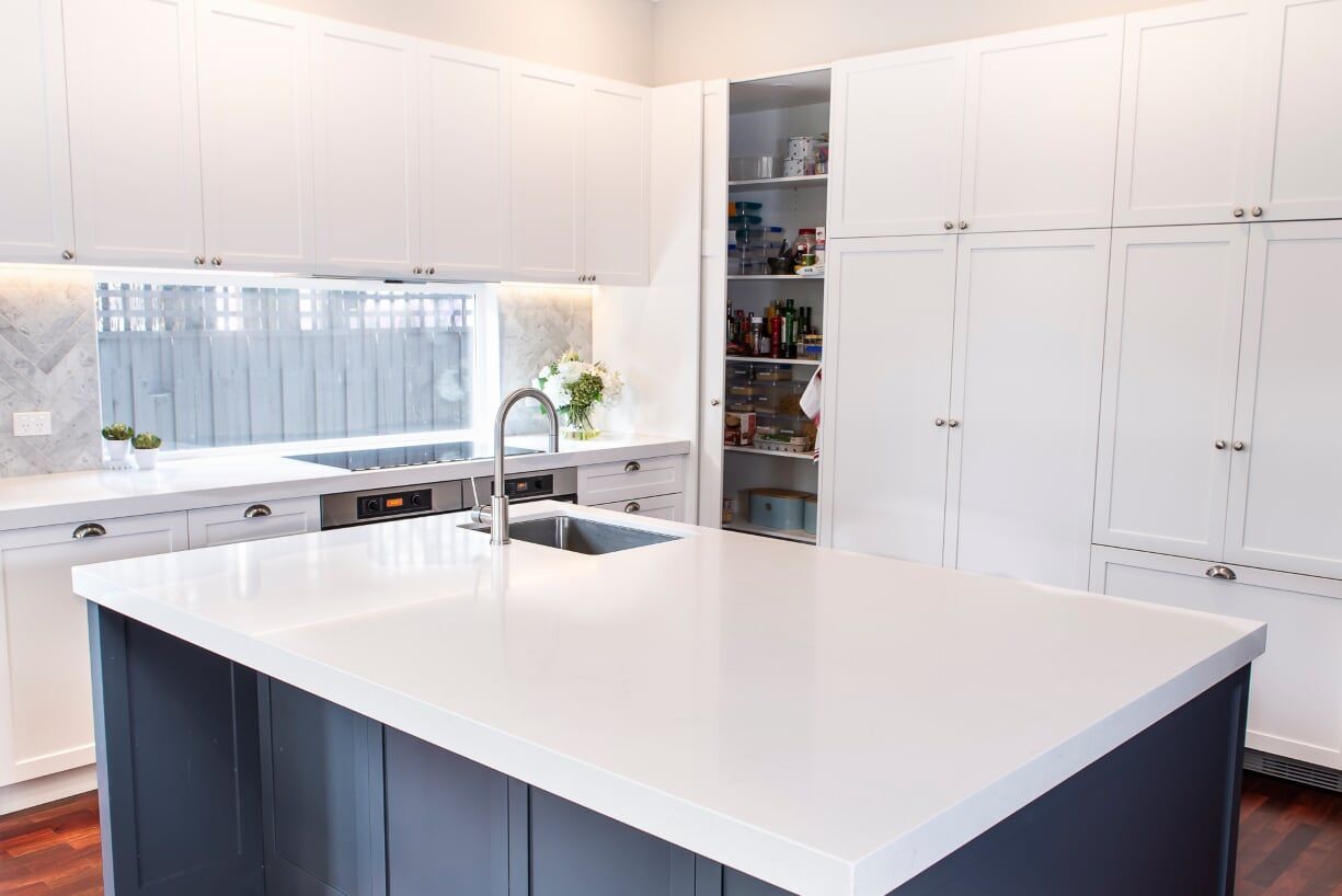 A kitchen with white cabinets, stainless steel appliances, hardwood floors and a large island.