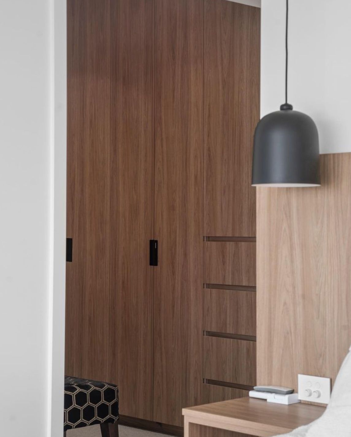 A bedroom with a bed, nightstand, cabinets and a pendant light.