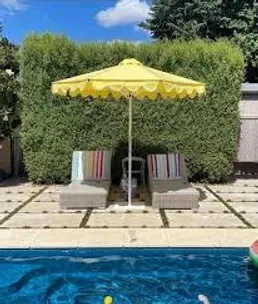 A swimming pool with a yellow umbrella and chairs next to it.
