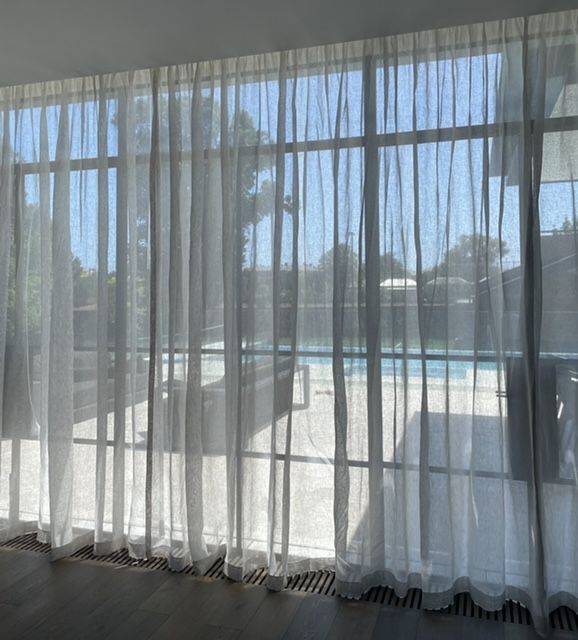 A room with sheer curtains and a view of a pool