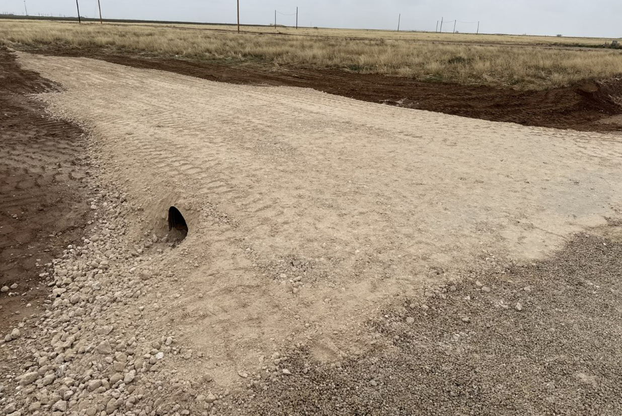 A dirt road going through a field with a hole in the middle of it.