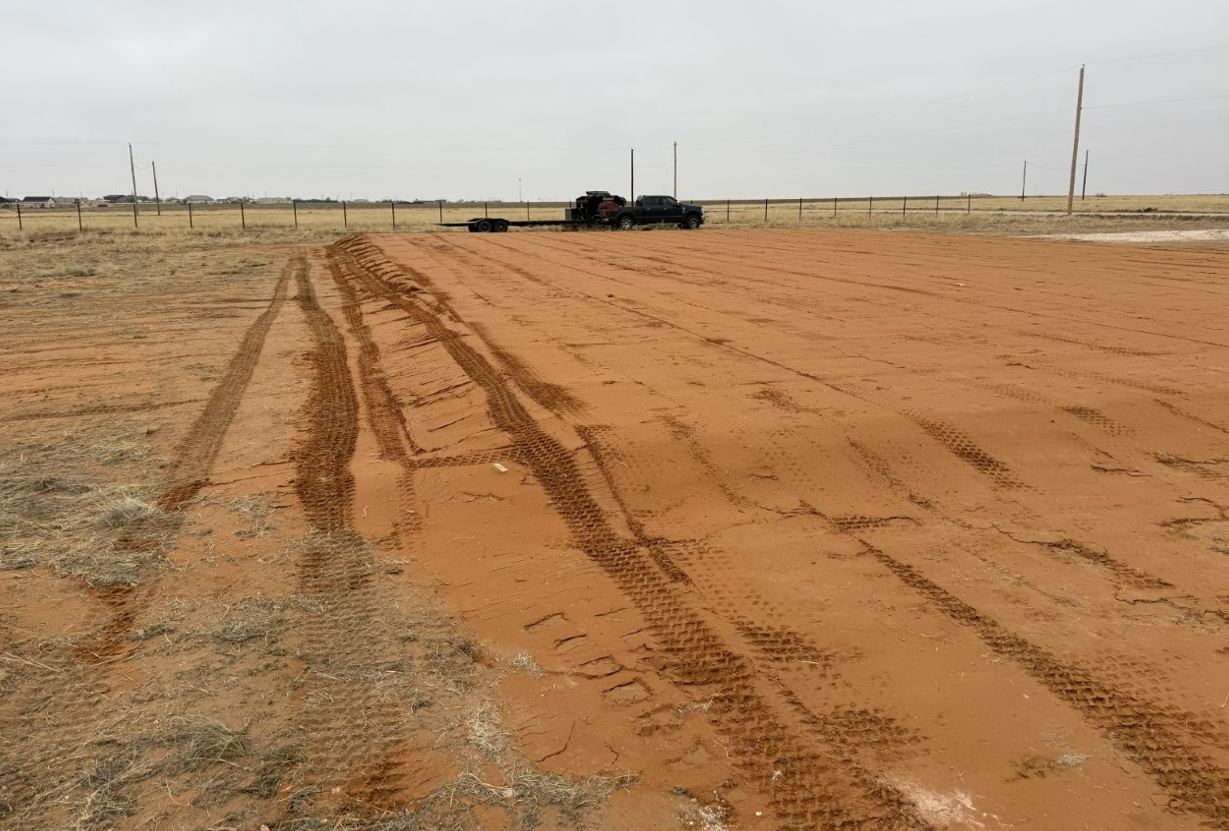A dirt road with tire tracks in it and a truck in the background.