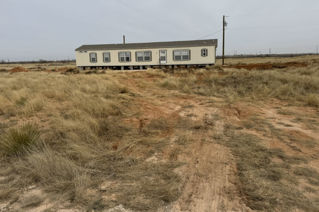A mobile home is sitting in the middle of a dirt field.