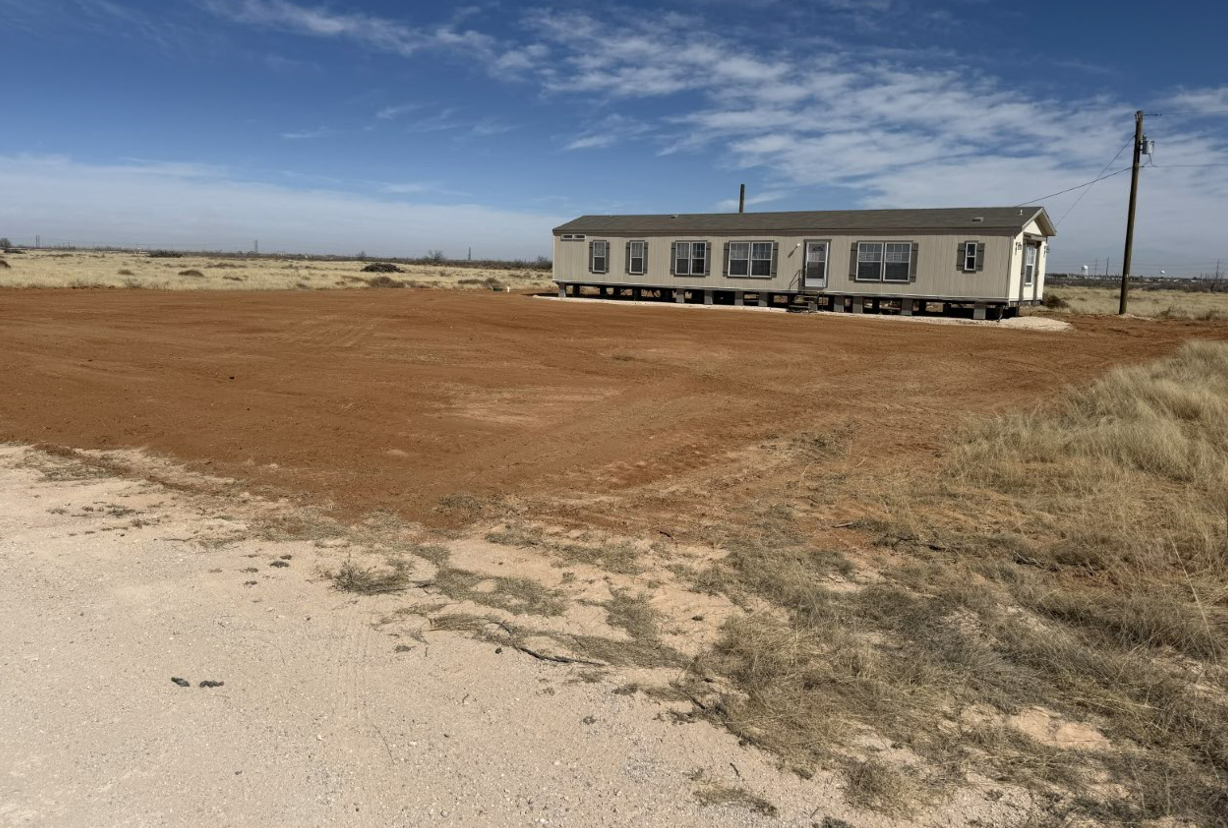 A mobile home is sitting in the middle of a dirt field.