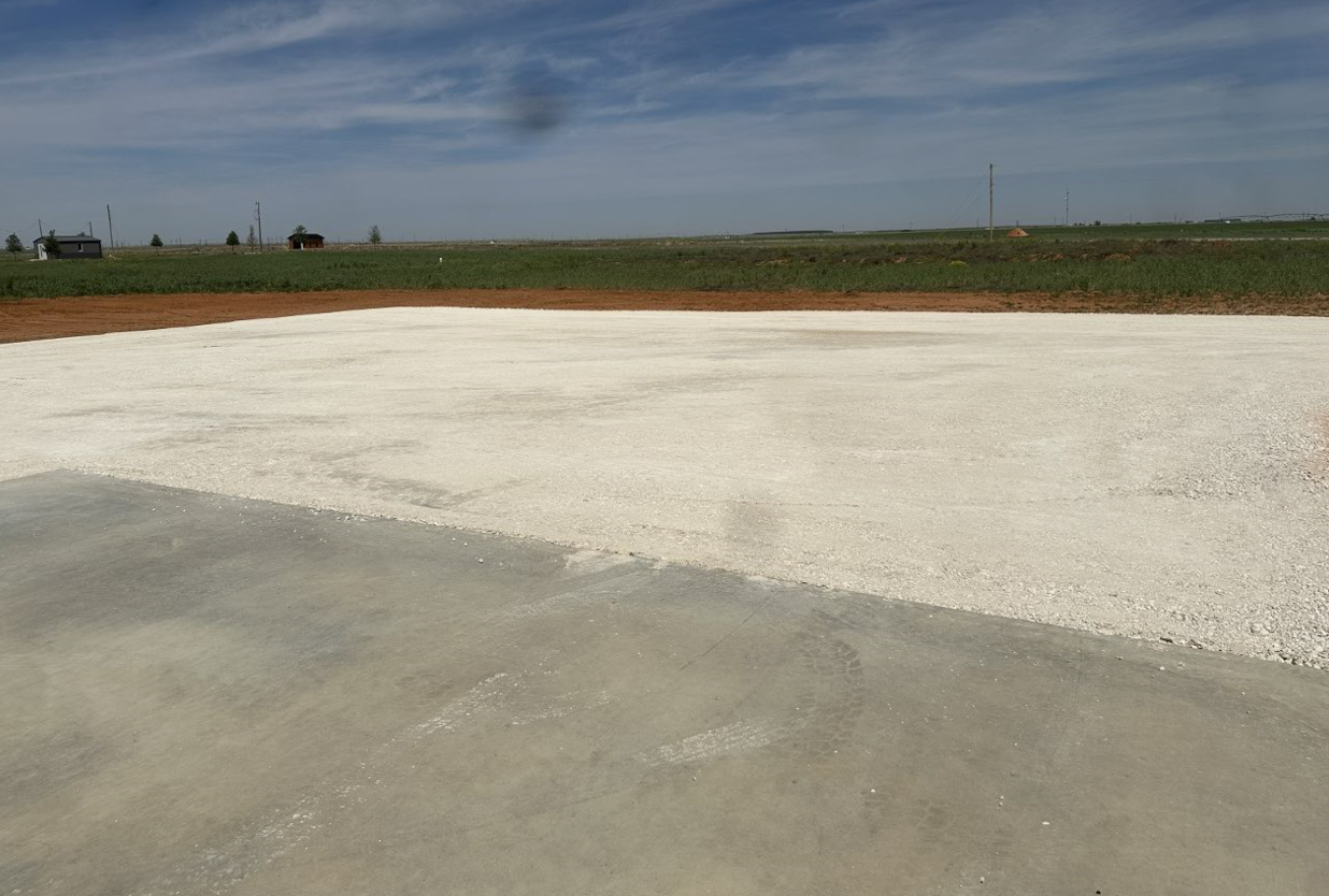 There is a lot of gravel on the ground and a field in the background.