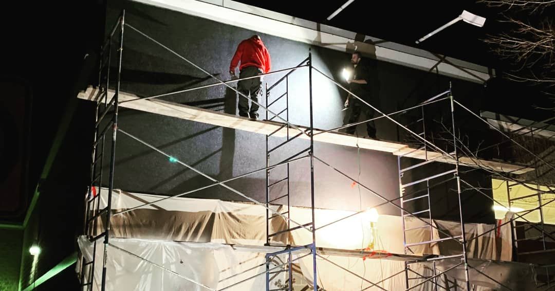 Un homme se tient sur un échafaudage au sommet d'un bâtiment la nuit.