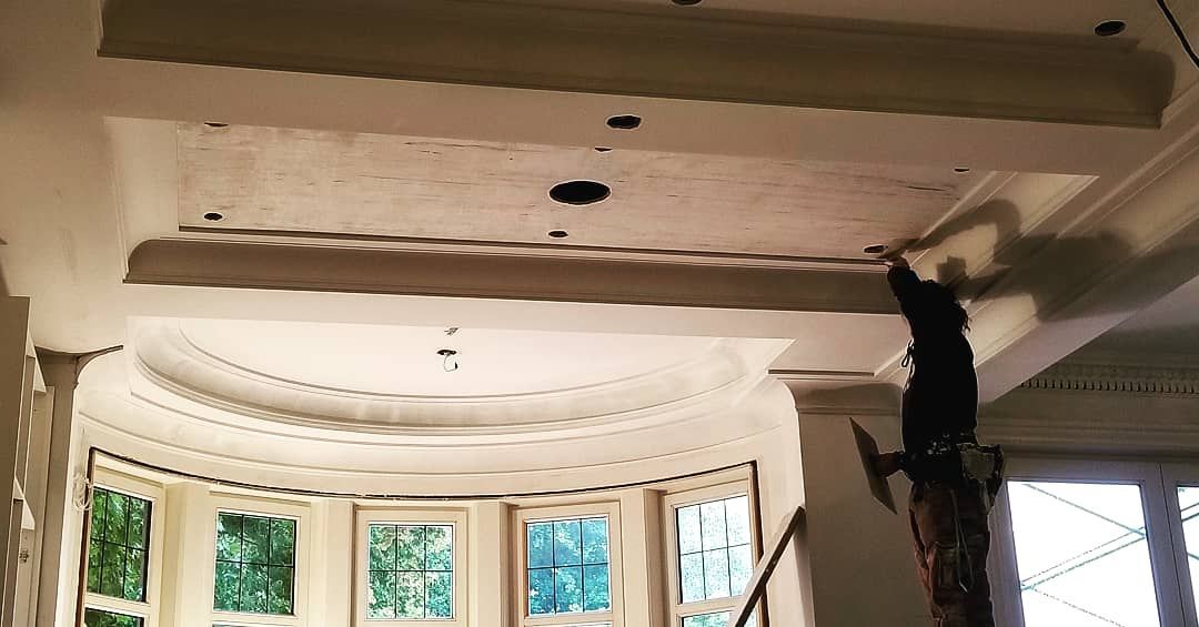 Un homme peint le plafond d'une pièce avec une fenêtre.