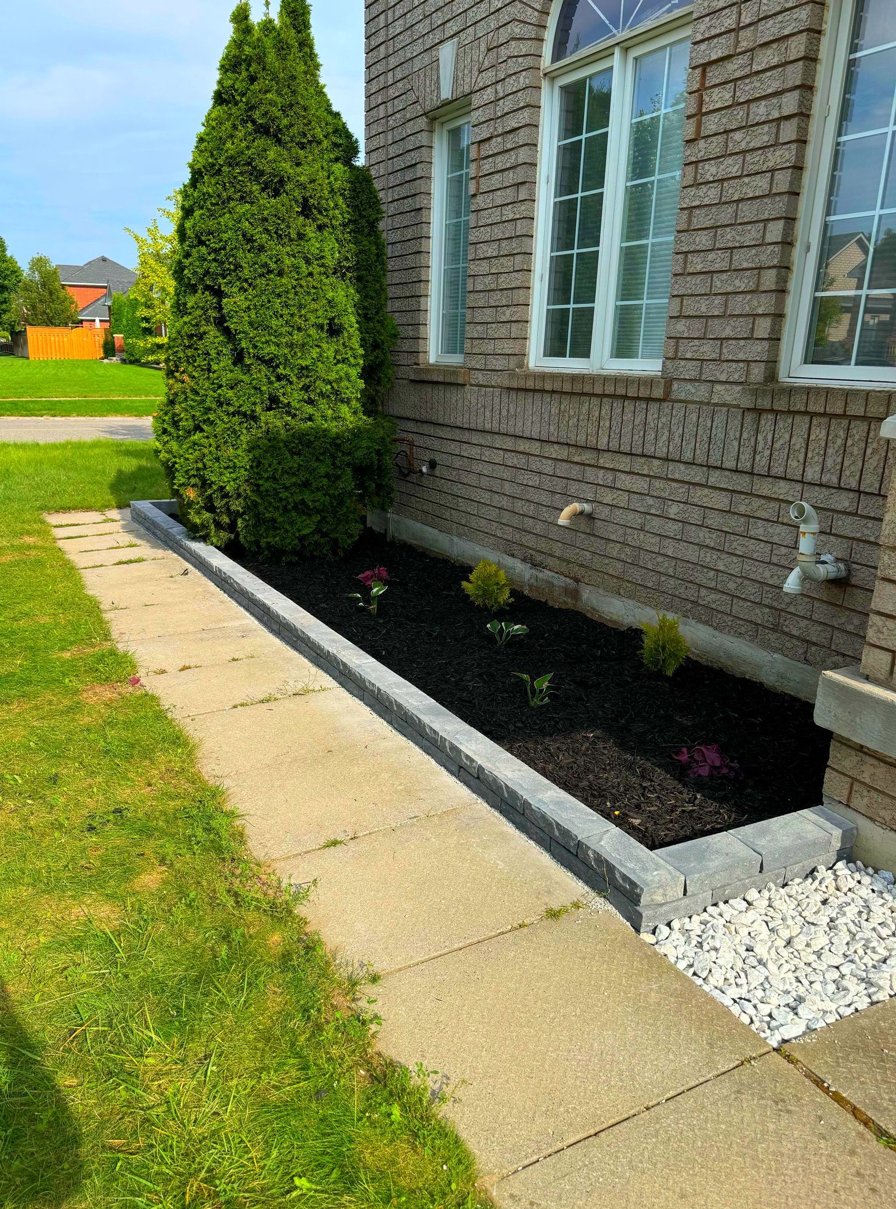 A brick house with a sidewalk and a garden in front of it.