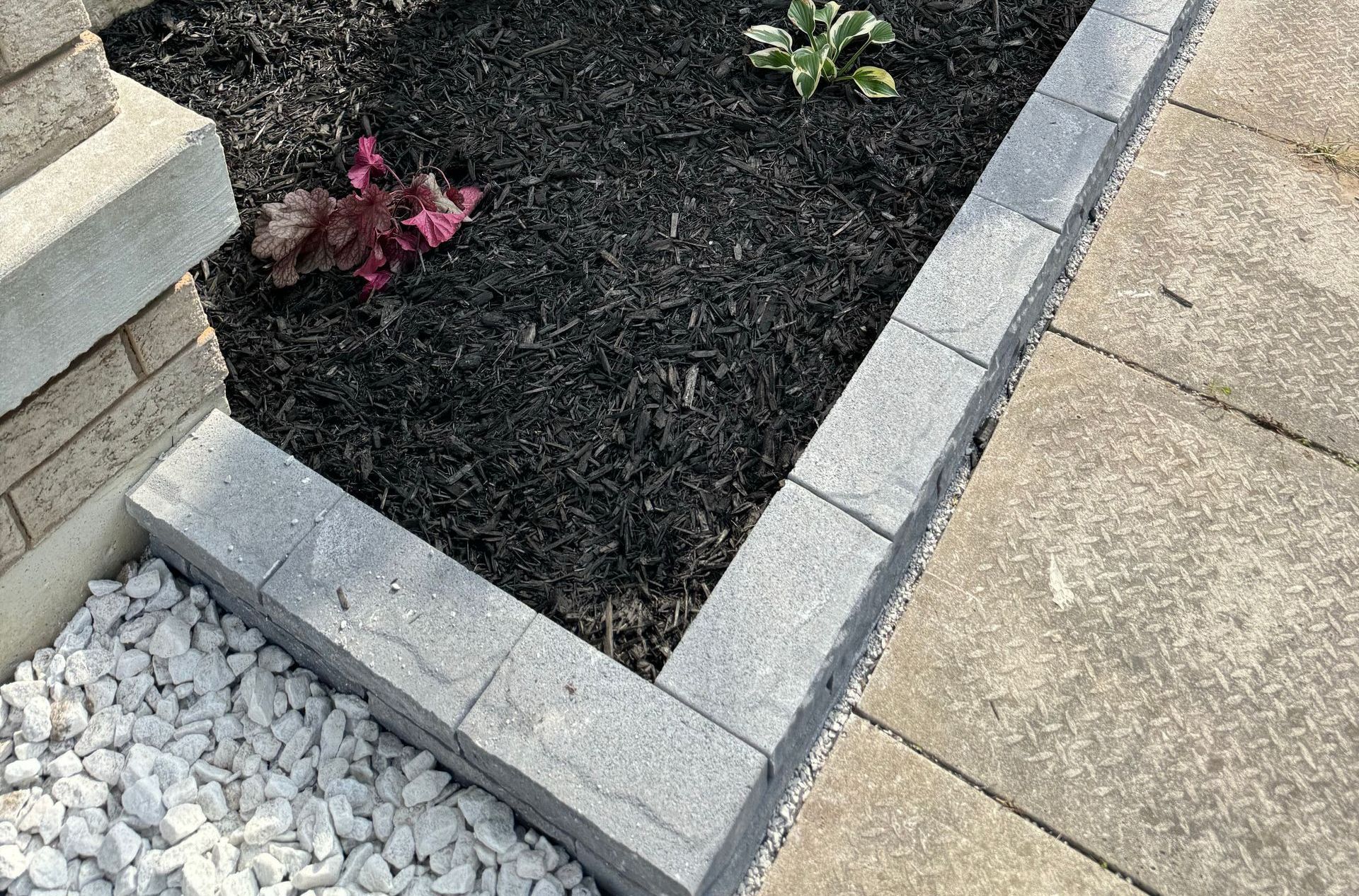 A garden with a brick border and white gravel next to a sidewalk.