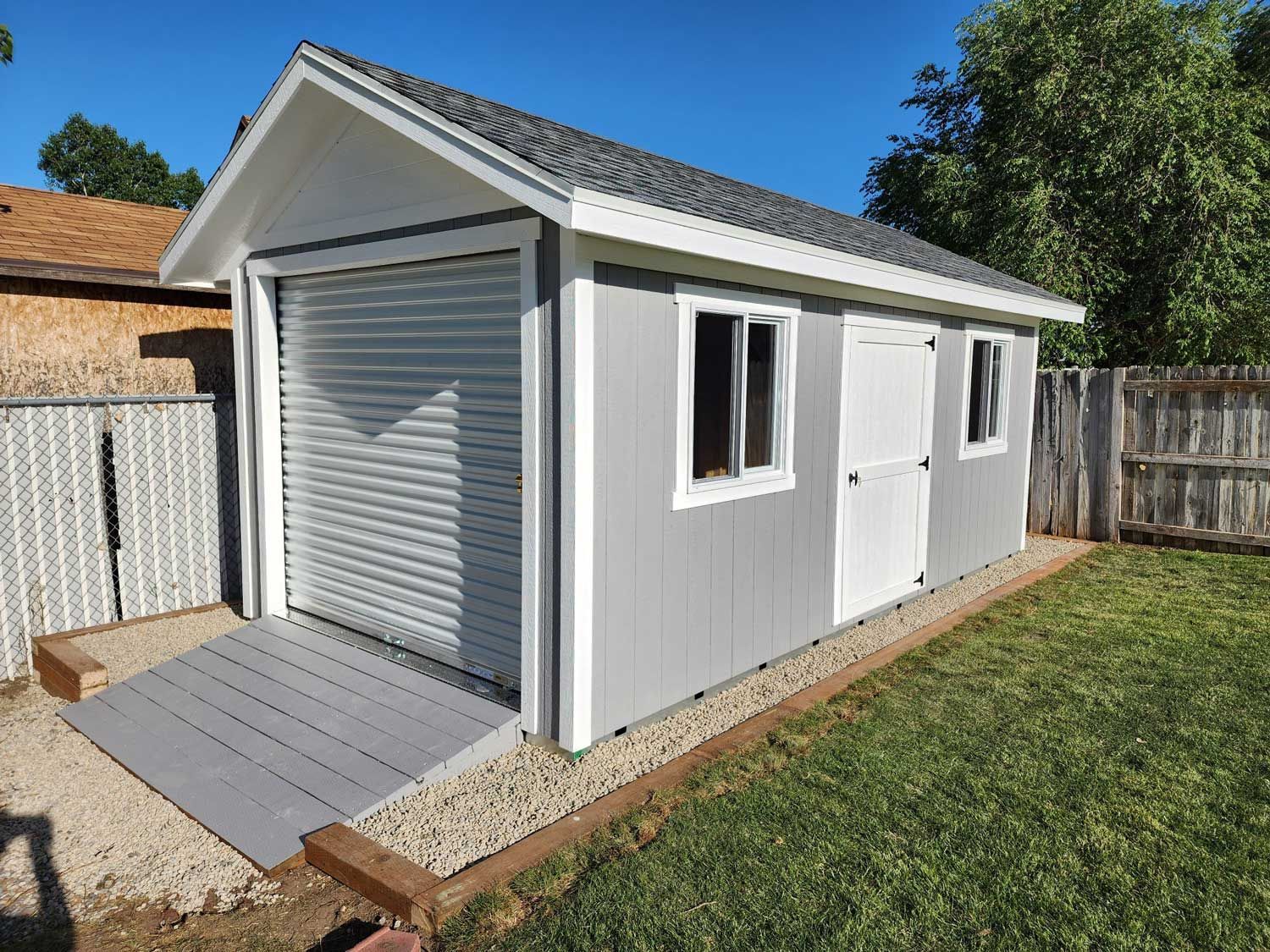 A shed with a ramp and a garage door in a backyard.