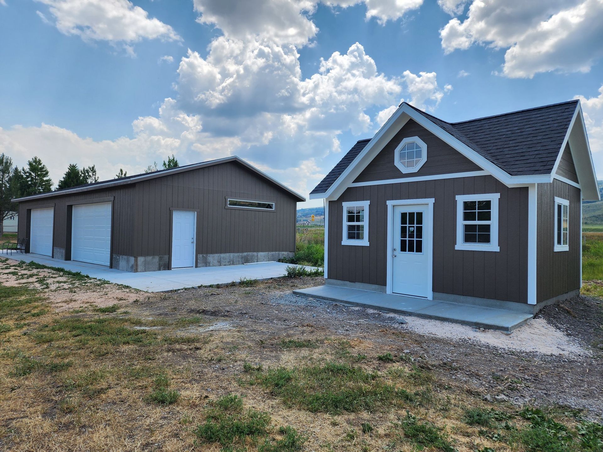 A Brown Garage and A Small House Are Sitting Next to Each Other in A Field.