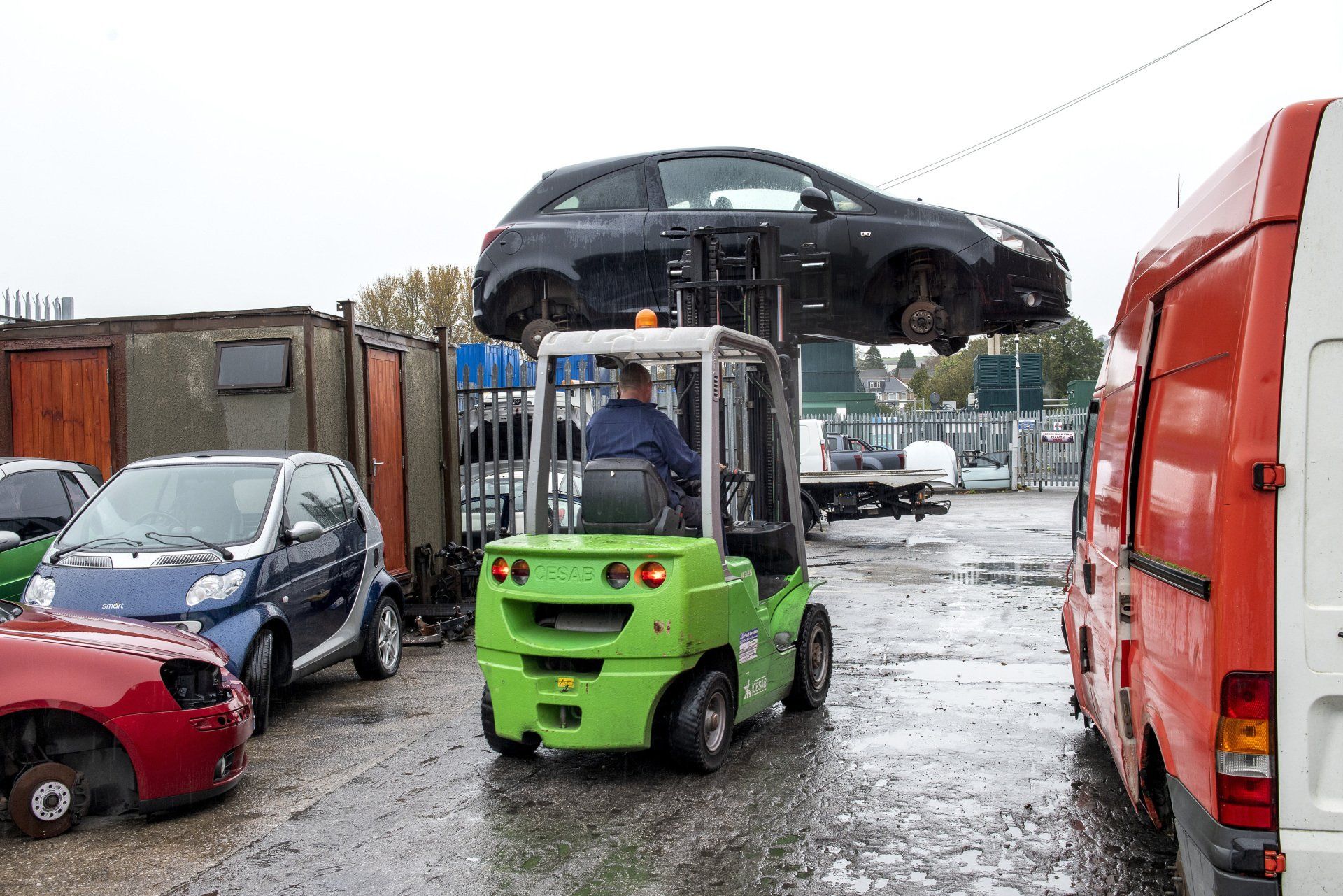 Man using a fork lift carrying a black scrap car