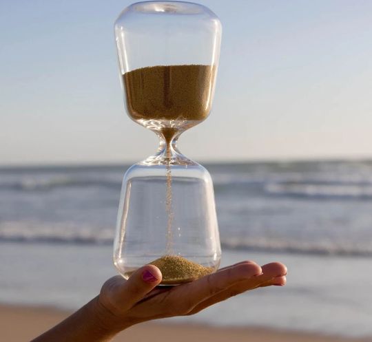 a person is holding an hourglass on the beach .