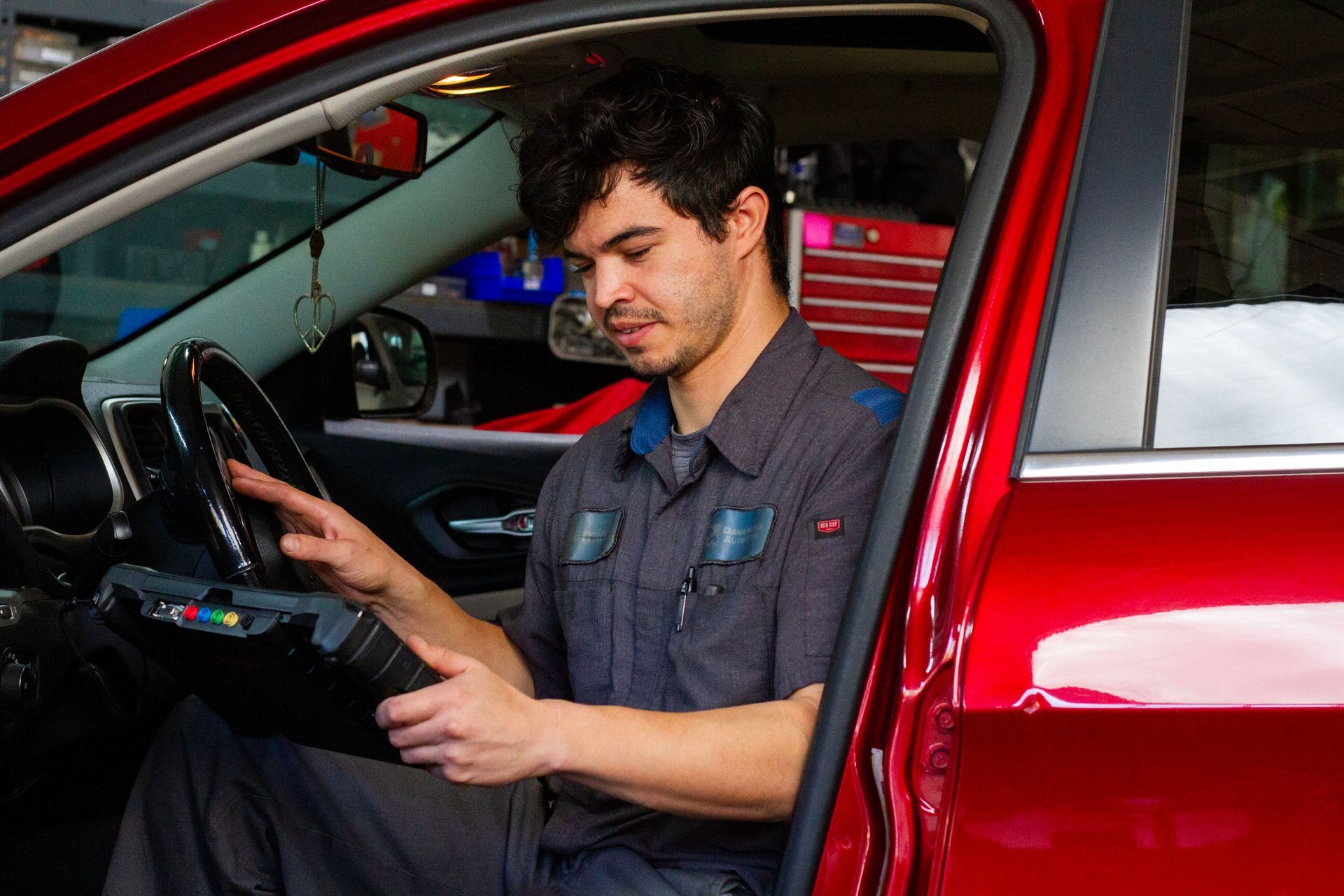 Auto mechanic using a diagnostic tool inside a red car. | Dana Meyer Auto Care