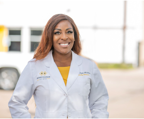 A woman in a white lab coat is smiling in front of a white van.