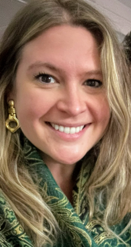 A woman wearing a green scarf and gold earrings is smiling for the camera.