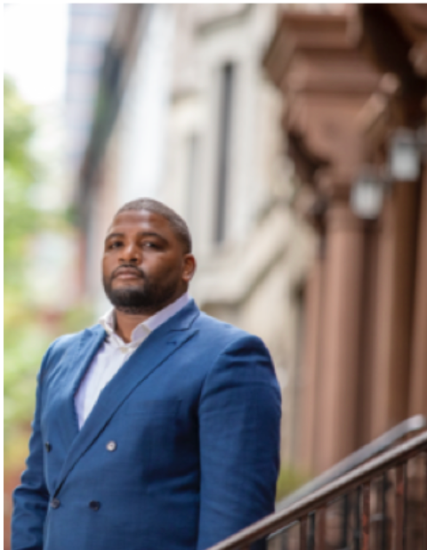 A man in a blue suit is standing in front of a building