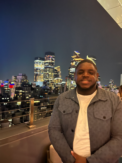 A man is standing in front of a city skyline at night.