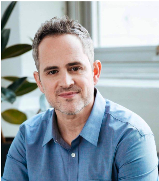 A man in a blue shirt is sitting in front of a window.