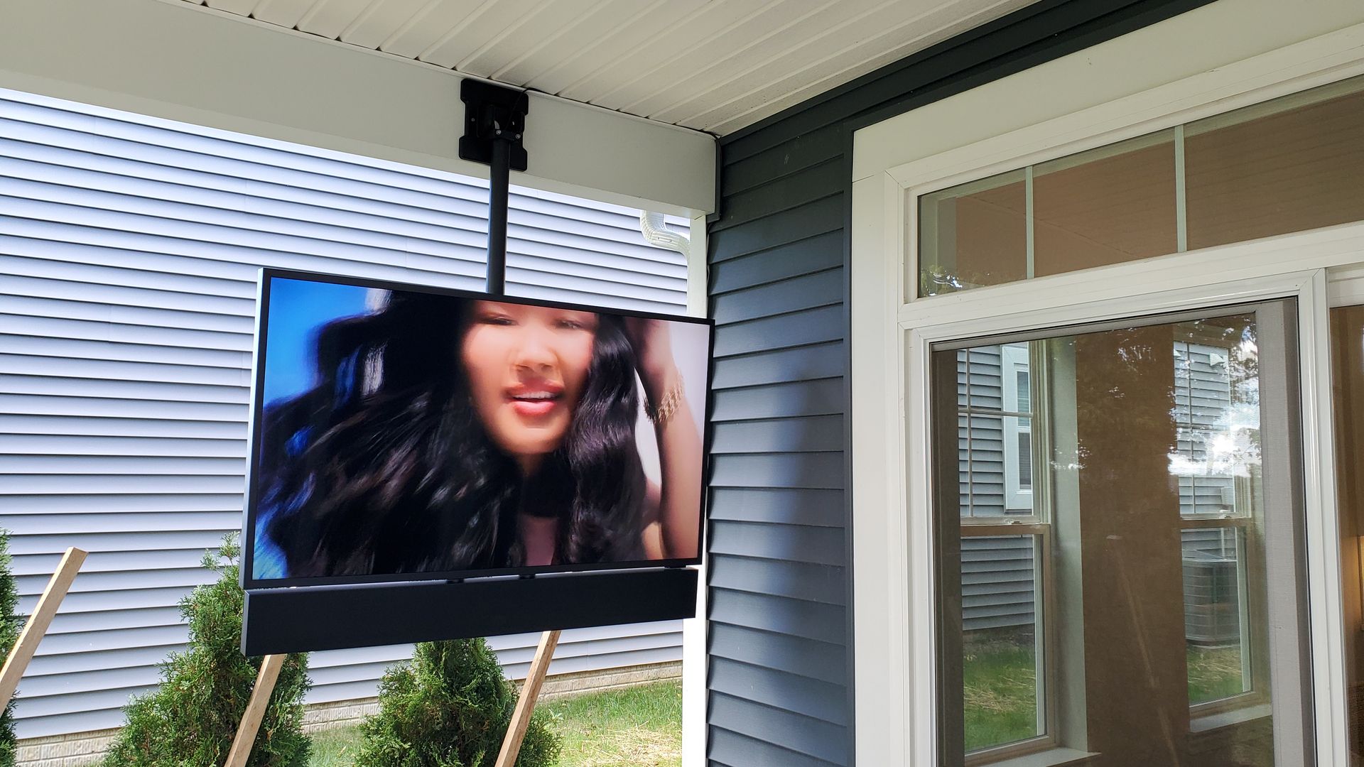 Outdoor television mounted on a porch ceiling, showing a person on the screen.
