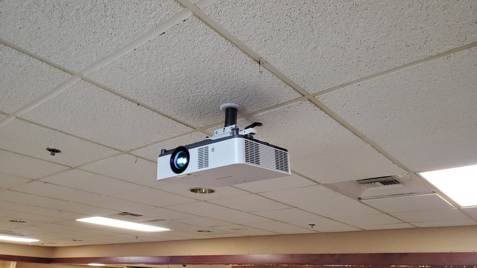 White projector suspended from a drop ceiling in a room.