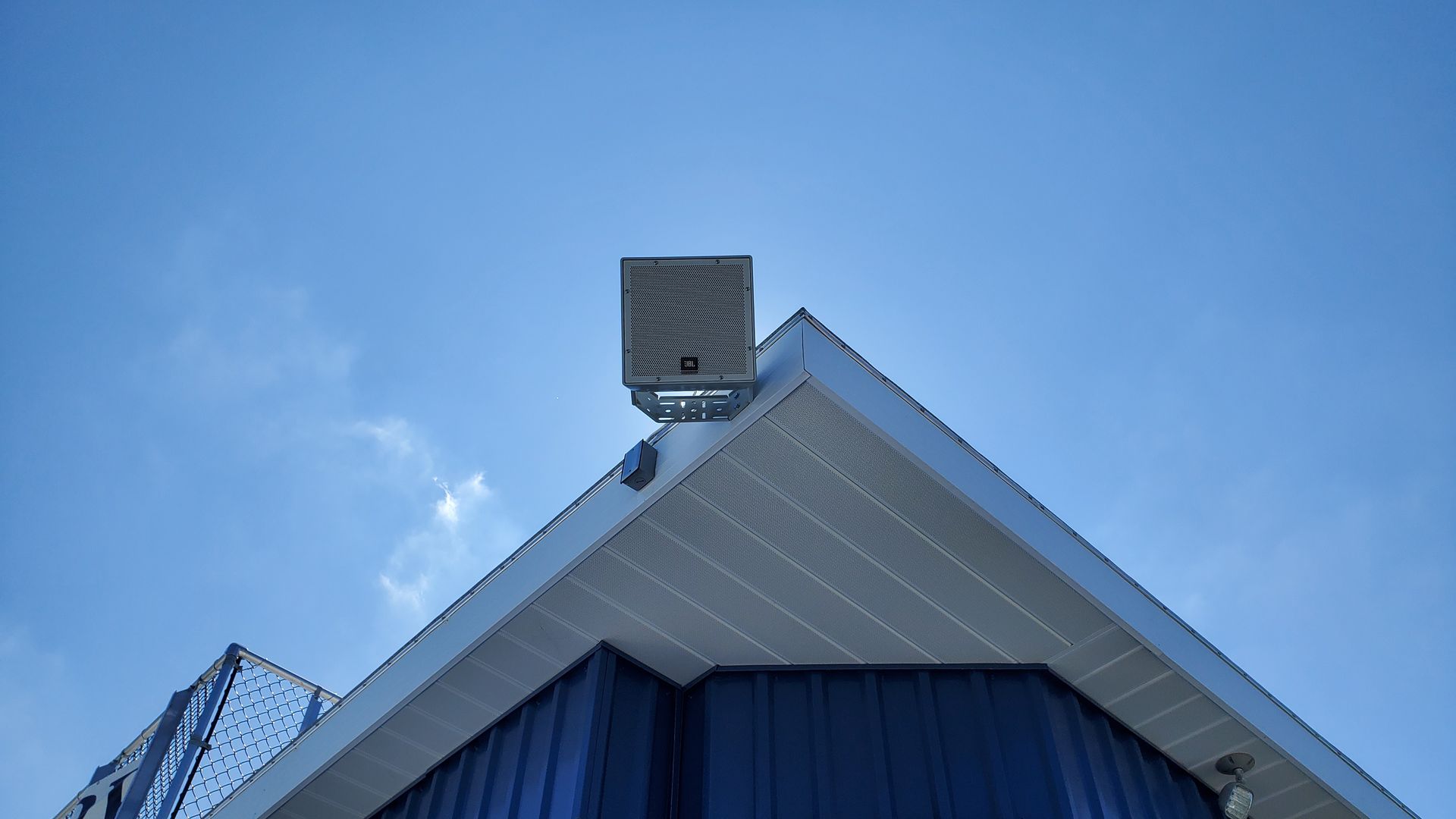 An outdoor speaker mounted on the pressbox of a football field. 