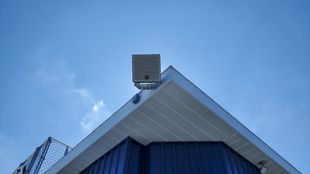 An outdoor speaker mounted on the pressbox of a football field.