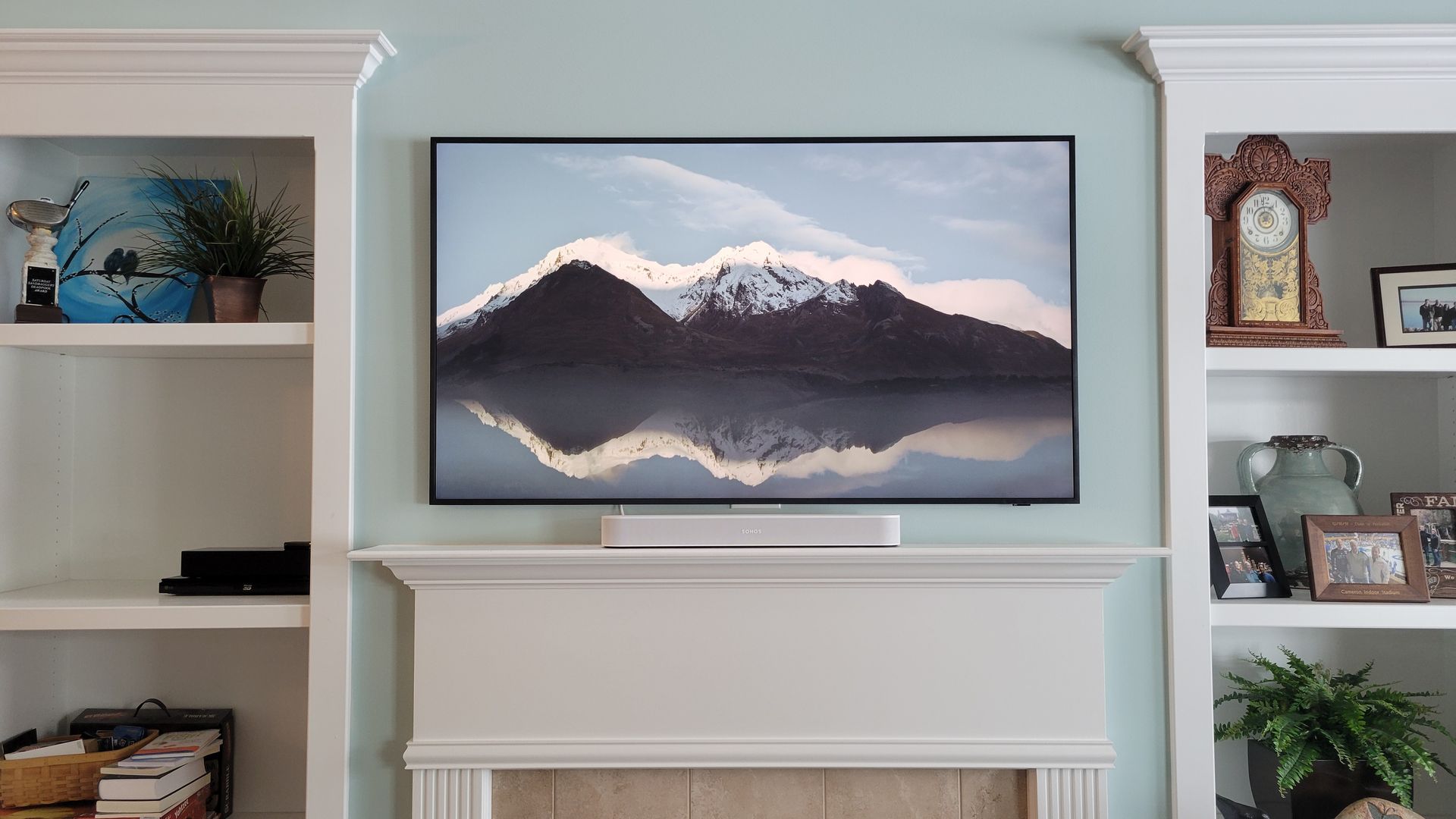 Built-in shelves with a samsung frame TV and soundbar mounted above a fireplace, displaying a mountain reflection scene.