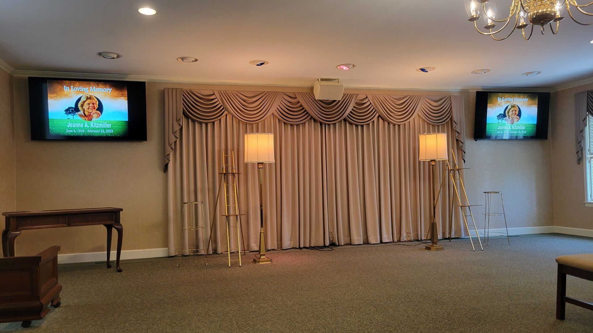 Funeral home interior with curtains, and two TVs displaying information from a video display system.