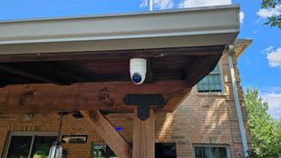 Security camera mounted under a wooden porch roof, in an outdoor patio.