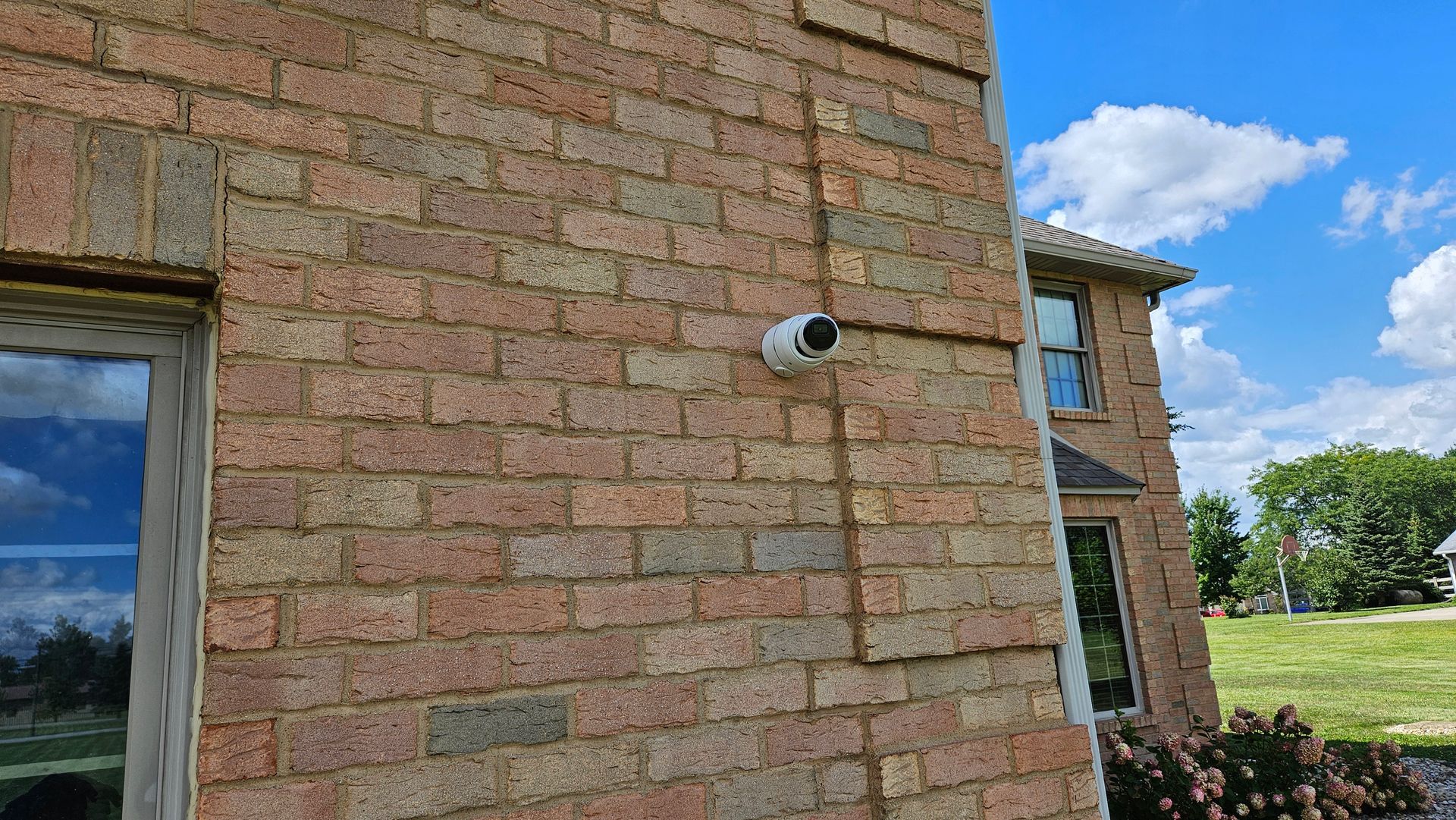Security camera mounted on a brick house exterior. Camera is white.