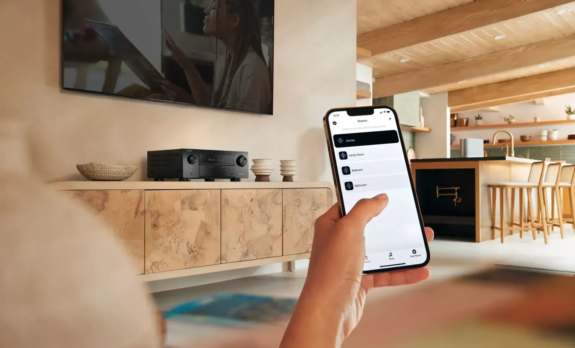 Person using a smartphone to control audio equipment near a TV in a modern living room.